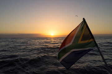 Close up of Flag of South Africa with sunset above the ocean in the background.