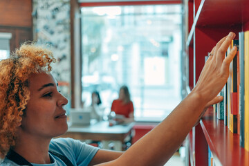 student or worker woman chooses a book from the bookshelf - people studying in the library -...