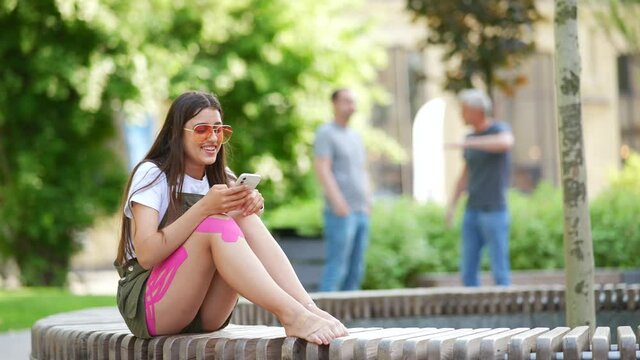 Pretty young woman using mobile phone app in city park