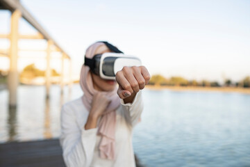 Unrecognizable Arab woman in VR goggles practicing boxing on embankment