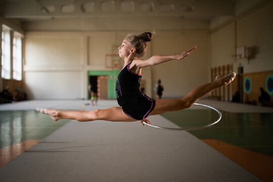 Girl gymnast jumping the splits with silver hoop in gym