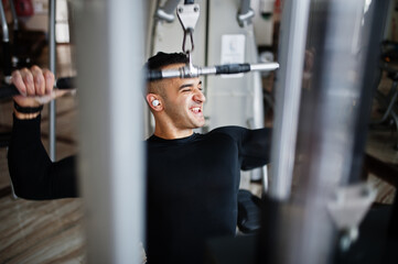 Fototapeta na wymiar Muscular arab man training and doing workout on fitness machine in modern gym.