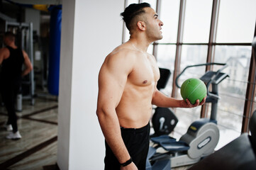 Muscular arab man training in modern gym. Fitness arabian men with naked torso doing exercises with ball.