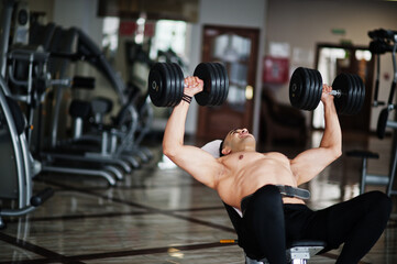 Fototapeta na wymiar Muscular arab man training in with dumbbells modern gym. Fitness arabian men with naked torso doing workout .