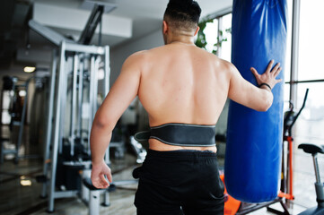 Fototapeta na wymiar Muscular arab man training in modern gym. Fitness arabian men with naked torso doing exercises with boxing bag.