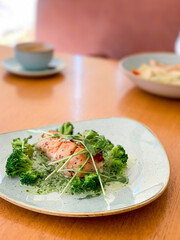 grilled salmon with broccoli in cream sauce, on a wooden table in a restaurant sitezen
