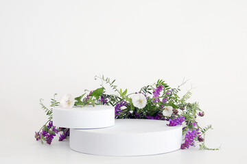 White podium on the white background with flowers. Podium for product, cosmetic presentation. Creative mock up. Pedestal or platform for beauty products.