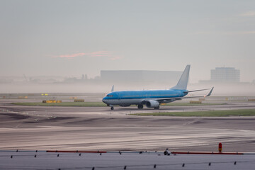 Airplane taxing on runway at Amsterdam Schiphol international airport during early morning mist