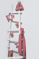 Christmas or New Year decor. A white wooden ladder with striped Christmas tree balls, hat and scarf hanging from it.