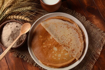 A traditional French Savory Buckwheat Galettes Bretonnes pancakes on a table with  flour, wheat plant and milk - obrazy, fototapety, plakaty