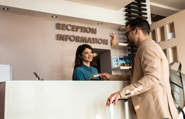 Guest pays for the stay at the hotel to female receptionist with a credit card at the reception.
