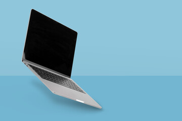 Laptop  computer with empty screen while levitating in the air on a blue background. Creative minimal background.