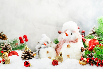 Christmas snow composition with two cute snowmen in hats and scarves in snowdrift and fir branches on gray background