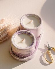Two natural handmade soy or coconut candles in purple concrete cups and ears of wheat. Crackling...