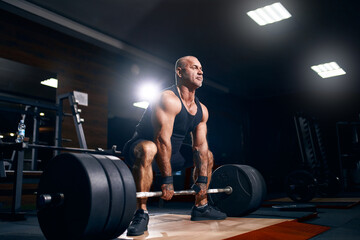 Fototapeta na wymiar Older sportsman exercising deadlift with barbell while on cross training in a gym. Bodybuilding 