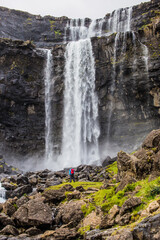 A hiker looking at Fossa,  the highest waterfall on the Faroe  
Islands