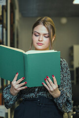 Girl is studying a book next to the rows of bookshelves.