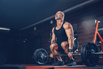 Fototapeta na wymiar Bodybuilder muscular man doing heavy deadlift exercise with weight while in gym in dark 