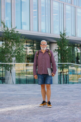 Naklejka premium an adult gray-haired man with a beard goes to the office to work. a senior businessman in a shirt and with a laptop is making a career in a large company. a stylish European talks on the phone with