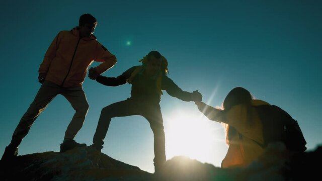 help team concept. team silhouette of climber stretching a helping hand to a friend. business teamwork success concept. silhouette business travel three tourists pull a helping sunlight hand