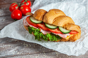 Breakfast of Fresh croissant with ham, cheese and salad leaf on white wooden background.