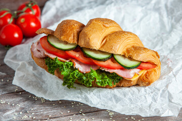 Breakfast of Fresh croissant with ham, cheese and salad leaf on white wooden background.