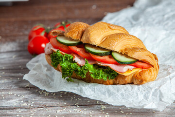 Breakfast of Fresh croissant with ham, cheese and salad leaf on white wooden background.
