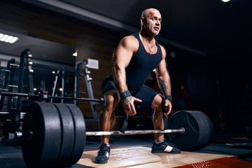Fototapeta na wymiar Older sportsman preparing to exercise deadlift with barbell while on cross training in a gym.