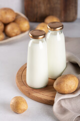 Bottles with vegan plant based milk. Dairy-free drink and potato tubers on gray table