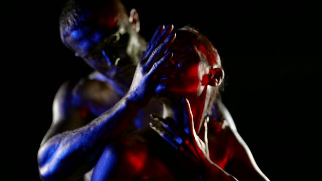 naked man and woman covered shiny dye are caressing each other in darkness