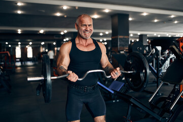 Fototapeta na wymiar Muscular older man working out in gym doing exercises with barbell at biceps. Bodybuilding concept