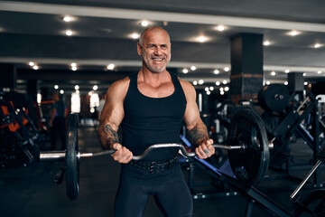 Muscular bald man working out in gym doing exercises with barbell at biceps. Bodybuilding concept