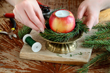 Woman shows how to make a Christmas decoration with apple, candle and branches of fir