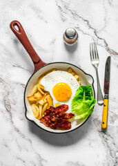 Delicious brunch, breakfast - potatoes hash, fried egg, bacon and green salad in a frying pan on a light background, top view