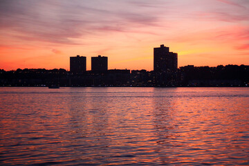 An orange sunset on the river Hudson behind the silhouette of the skyscrapers