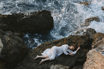 woman in long white dress wet hair lying on a rocky cliff landscape