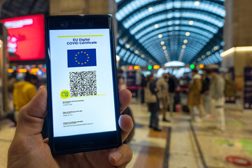 Woman showing on smartphone EU Digital Covid Certificate with quad code. Train station background.