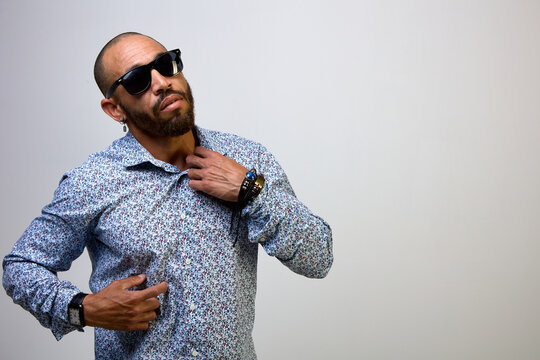 Portrait of a cool Latino man with a beard, wearing black sunglasses and a shirt on a white background. Brutal guy sexually holds on to the collar of his shirt