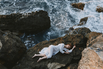 sensual woman in a white dress lying on a stone in a white dress landscape