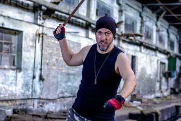 Young rebel in abandoned factory hall with a metal bar in his hand, threatening and looking with...