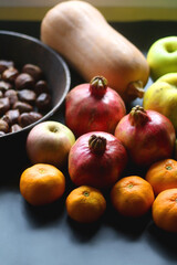 Pan with chestnuts, butternut squash and various fruit on dark background. Selective focus.