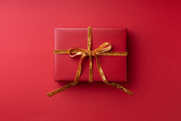 Red gift box tied golden ribbon on red background.