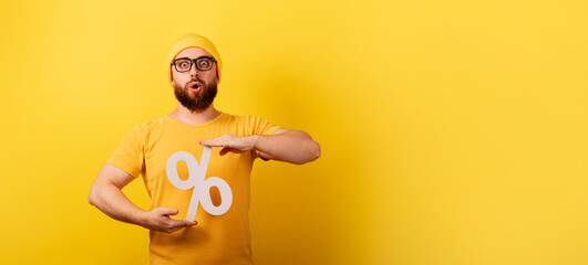 shocked man hold 3d percentage sign over yellow background, discounts with high interest, panoramic layout with space for text - obrazy, fototapety, plakaty