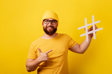 smiling bearded man pointing on hashtag over yellow background