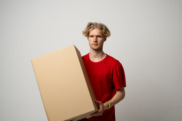 Delivery Service Concept. Male worker in red uniform holding cardboard box isolated over white studio background.