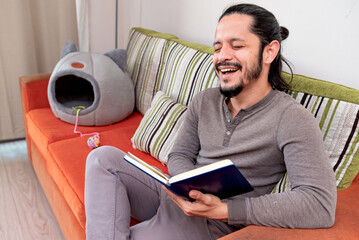 Young man reading a book at home sitting on the couch in the living room