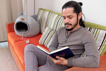 Young man reading a book at home sitting on the couch in the living room