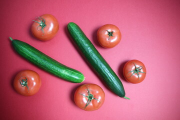 Ripe red fresh tomatos and green cucumbers on red background