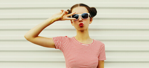 Portrait of stylish young woman blowing her lips sending sweet air kiss with red lipstick wearing a striped t-shirt with cool hairstyle on white background