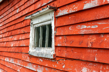 The exterior wall of a textured grungy wooden worn red building. The wall has a small window with...